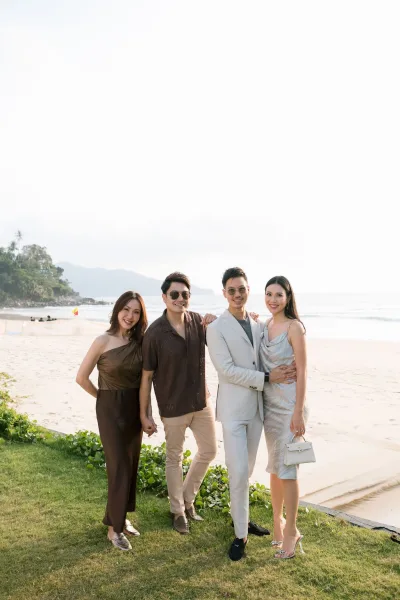 Wedding guest portrait featuring beach wedding guest attire as guests pose by the ocean shoreline, one wearing sunglasses in coastal light.
