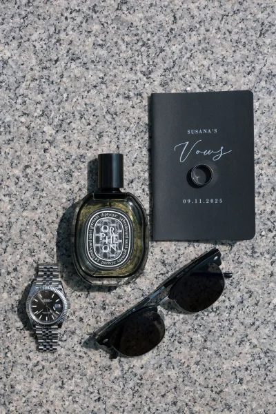 Groom details arranged as a flat lay featuring a vow book with ring on a textured granite surface, with a clean, minimal look.