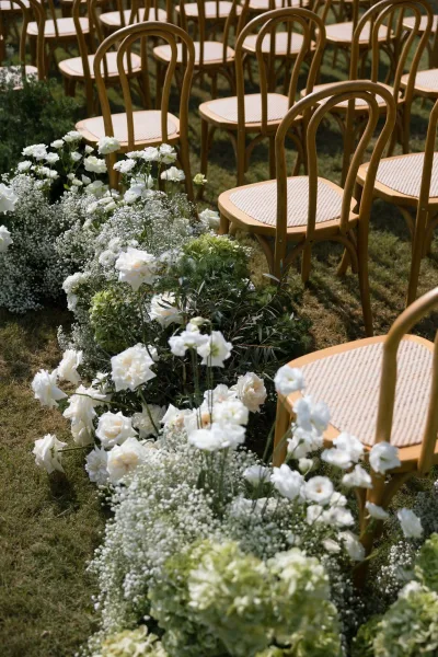 Ceremony aisle flowers form soft aisle meadow florals flanking bentwood chairs, creating a low, romantic path down the center.