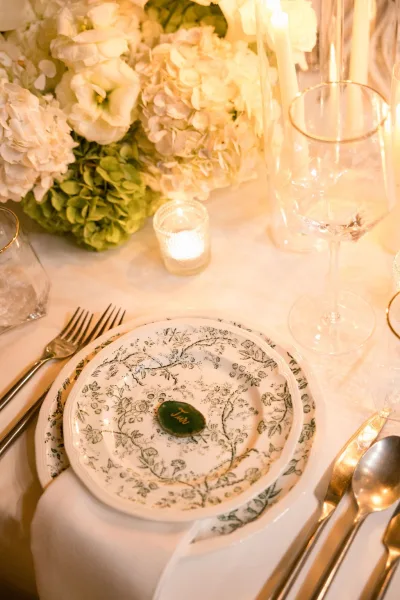 Wedding place setting with patterned china plates and gold rim glassware, set neatly on white table linen