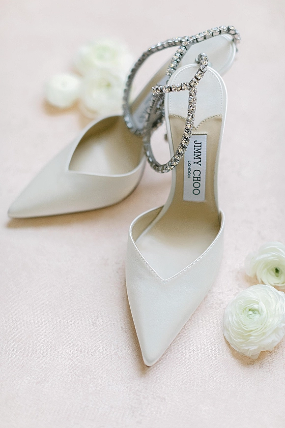 Bridal shoes with jimmy choo bridal shoes styling, white satin pointed toe heels and crystal ankle straps on blush fabric with ranunculus flowers