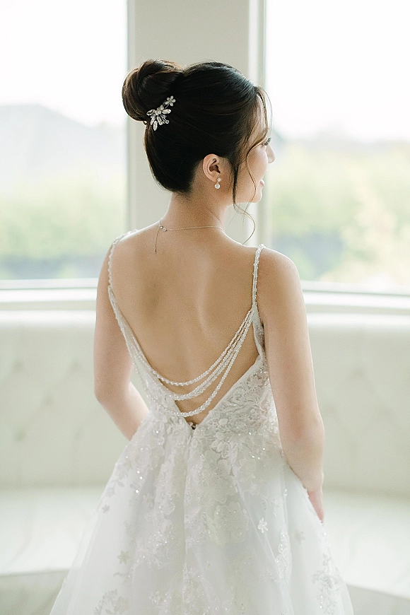 Bridal portrait of a bride from behind in a backless wedding dress with beaded straps and draped pearl back necklace by window light