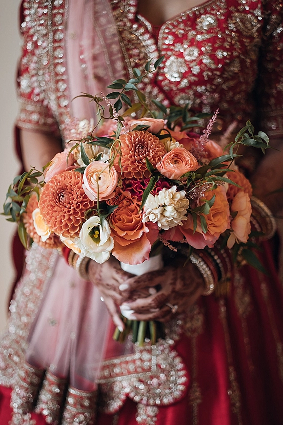 Bridal bouquet of peach wedding bouquet blooms and coral bridal bouquet flowers held in hennaed hands with bangles against a neutral wall