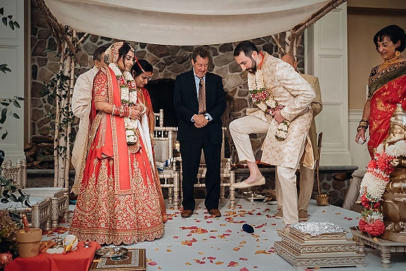 Wedding ceremony moment during a hindu wedding ceremony as bride in red lehenga and groom in sherwani exchange floral garlands under canopy