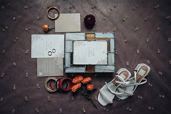 Wedding invitation suite wedding flat lay with rings, bangles, orange roses, and white strappy heels on embroidered fabric with beadwork