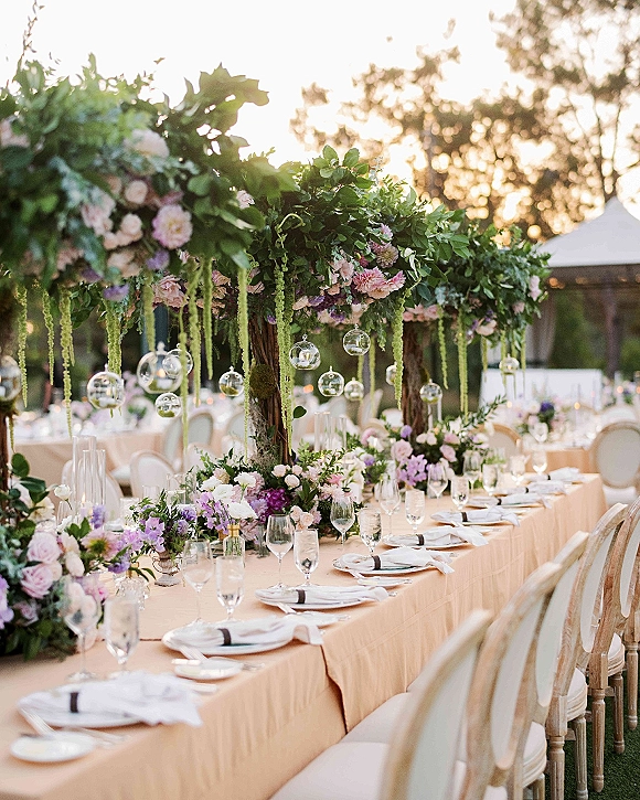 Reception tablescape with outdoor reception table styling, lush floral centerpiece, taper candles and hanging glass orbs under a white tent at sunset