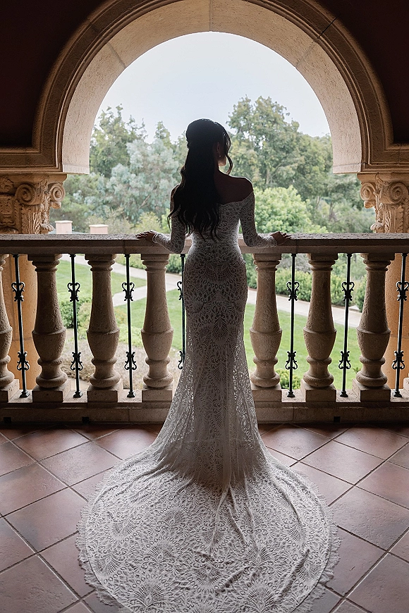Bridal portrait showing back view wedding dress with a cathedral train spread on an arched stone balcony overlooking garden paths