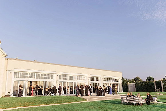Wedding reception venue with outdoor wedding cocktail hour drinks, lounge sofas on a lawn beside a modern white building with glass doors