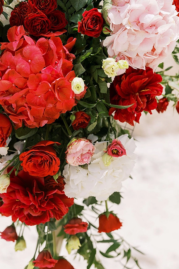 Wedding floral arrangement with red and pink wedding flowers, red roses, hydrangea and greenery on a clean white surface