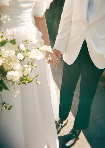 Couple holding hands, a tender wedding hands detail highlighting her wedding ring as they pause together in an elegant moment.