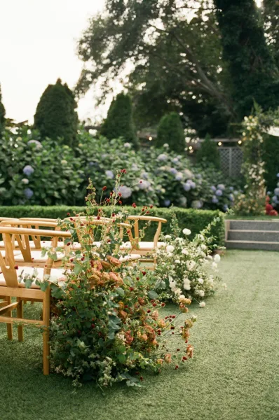 Ceremony aisle design with lush florals amid hedges and hydrangeas on the lawn in a garden ceremony setup.