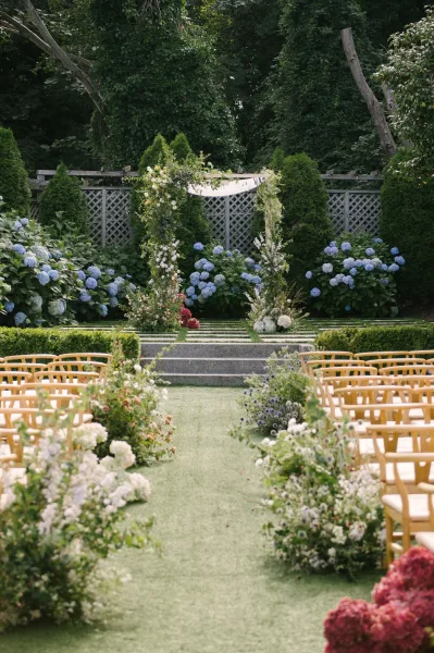 Ceremony aisle design for a garden wedding ceremony, lined with hydrangea aisle florals, facing a lattice fence amid garden trees.