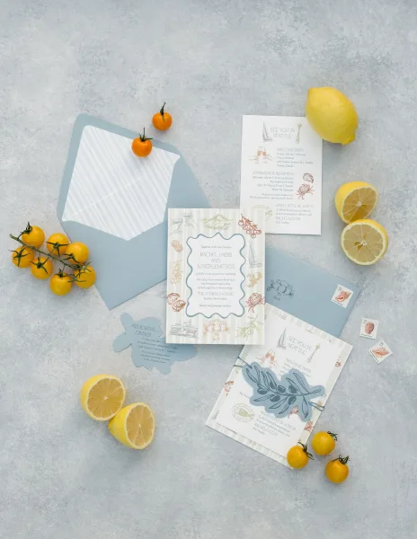 Invitation suite of blue and white wedding invitations styled with a lemon accent on a gray stone surface