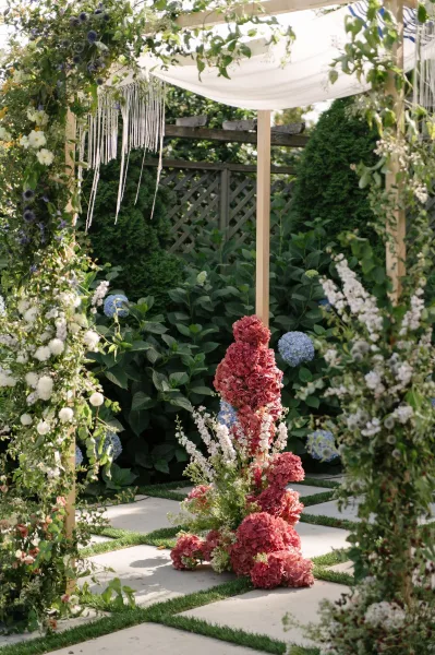 Wedding chuppah anchors garden ceremony decor, its fabric canopy soft against garden shrubs and a lattice fence over stone pavers.