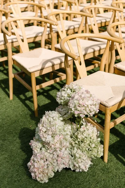 Ceremony seating with outdoor ceremony chairs in neat rows of wishbone chairs flanking a simple aisle on a sunlit grass lawn.