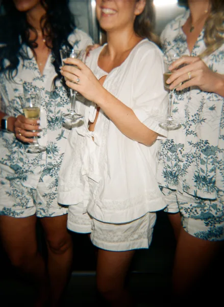 Getting ready moment as the bride with bridesmaids raise champagne flutes against a dark indoor backdrop