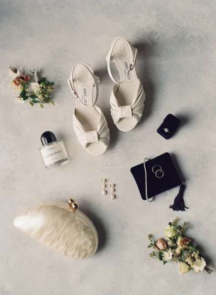 Bridal accessories in a wedding detail flat lay, featuring a blue velvet ring box, arranged on a textured grey stone surface.