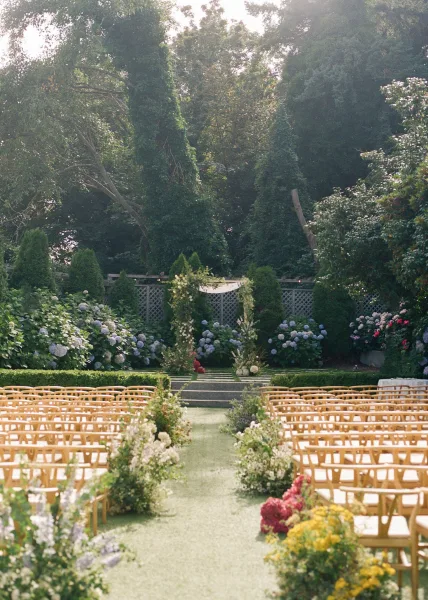 Garden ceremony setup with outdoor ceremony decor featuring hydrangeas lining the aisle, framed by hedges and a lattice fence backdrop.