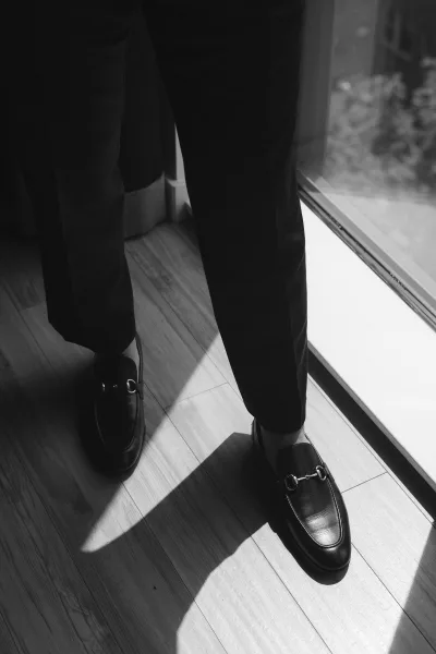 Groom shoes—black leather loafers with gleaming horsebit hardware, neatly aligned and polished for a refined wedding detail.