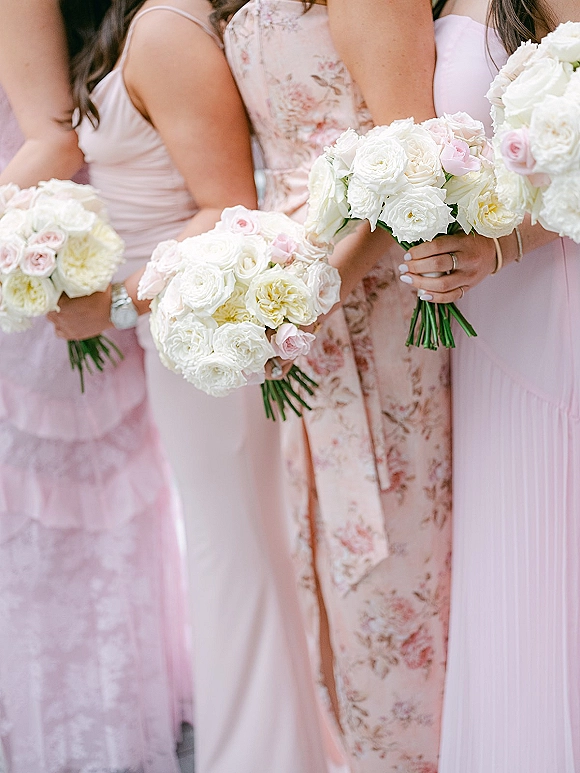 Bridesmaid bouquets of white roses with pale pink roses held by bridesmaids in mismatched blush dresses, showing jewelry and manicured nails