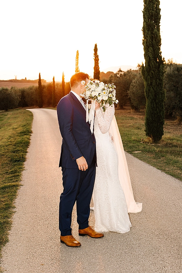 Wedding couple portrait of bride and groom kissing behind a white and green bouquet with ribbon streamers on a sunset country road