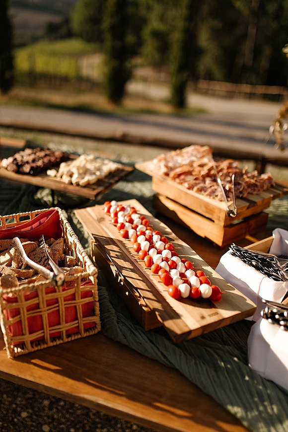Wedding appetizer table with wedding cocktail hour food, caprese skewers and bread basket on wood boards in sunlit outdoor setting