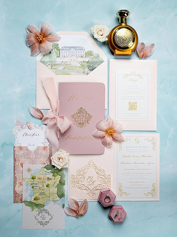 Wedding invitation suite with blush pink invitations, gold foil lettering, and pink ribbon bow arranged as a flat lay on blue backdrop