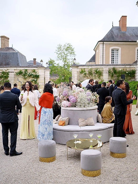 Wedding cocktail hour lounge seating with round banquette sofa, hydrangea centerpiece and martini glasses in an ivy-walled stone courtyard under string lights