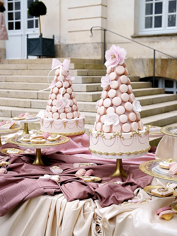 Wedding dessert table with a macaron tower wedding centerpiece, pink ribbon bow and gold stand set on stone steps outside a building facade