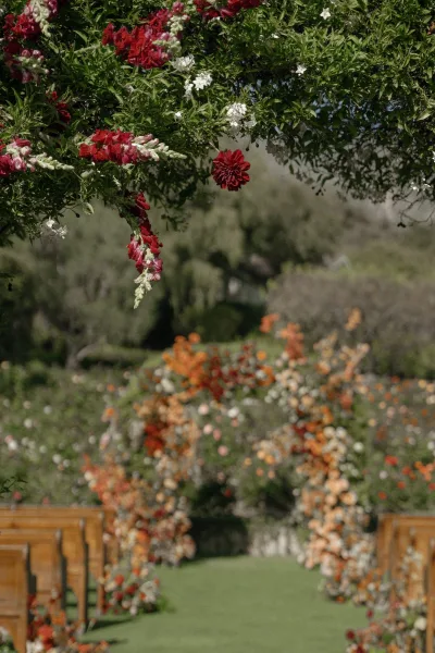 Ceremony aisle decor with an outdoor ceremony aisle of wooden chairs leading to a floral arch with hanging arrangements amid garden greenery and trees