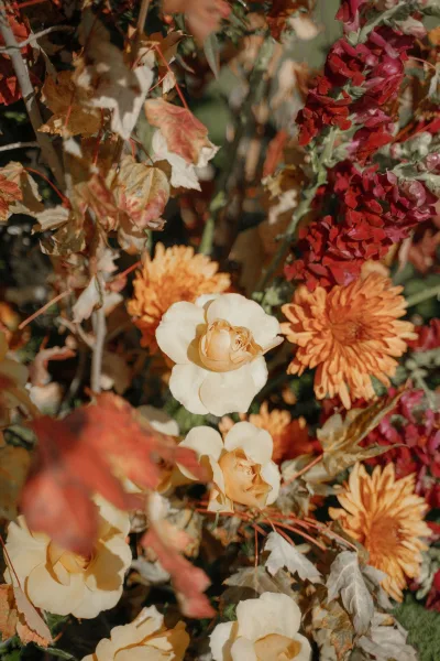 Wedding florals with fall wedding flowers in rust and cream roses, chrysanthemums, and autumn leaves, arranged against garden foliage