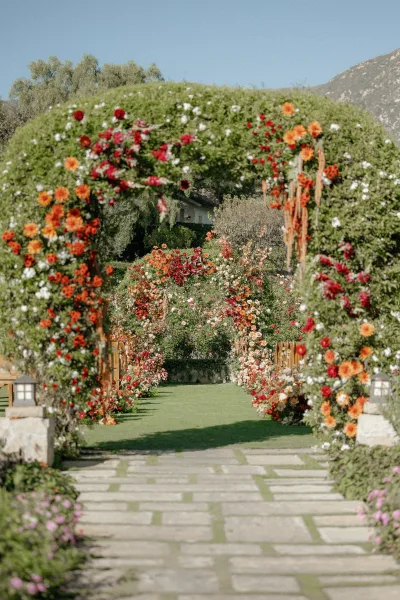 Ceremony aisle decor on an outdoor ceremony aisle with floral arch, lanterns, and garden flowers along stone pavers beneath mountains