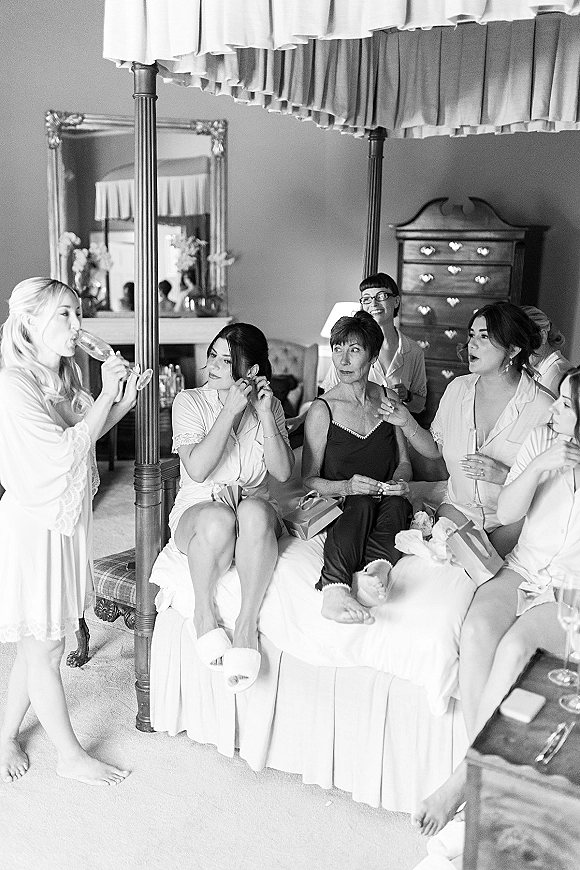 Bridal party getting ready in matching pajamas, raising champagne flutes on a four-poster bed in a cozy bedroom setting