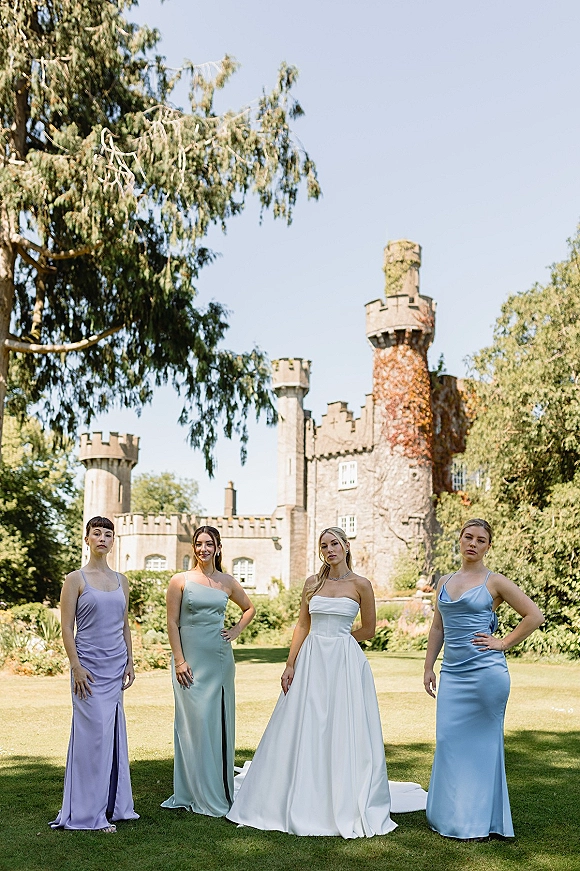 Bridesmaid dresses in pastel bridesmaid dresses, mix-and-match satin gowns with earrings on a castle lawn under blue sky