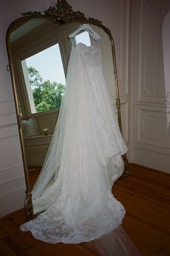 Wedding dress, lace wedding dress hanging on a hanger with veil beside an ornate gold mirror in a bright paneled room by a window
