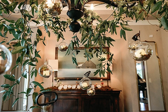 Hanging greenery decor with a greenery chandelier wedding of glass globe terrariums and floating candles, suspended over a sideboard in an indoor room