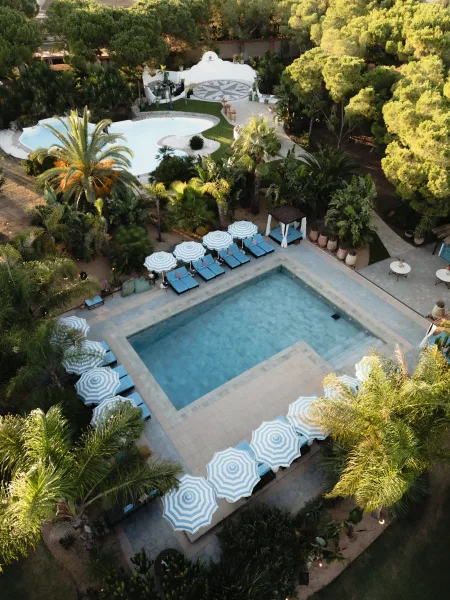 Outdoor wedding venue with a poolside wedding venue ceremony arch, striped umbrellas and loungers beside a palm-lined lawn and pathways
