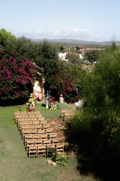 Outdoor ceremony setup with wood folding chairs facing a floral arch, petal-lined aisle and lantern on a garden lawn with mountain views