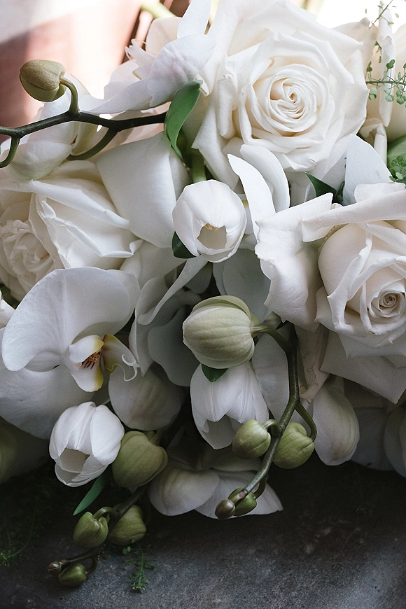 Bridal bouquet of white roses and orchids with greenery and trailing stems, styled on a textured stone surface for a clean look