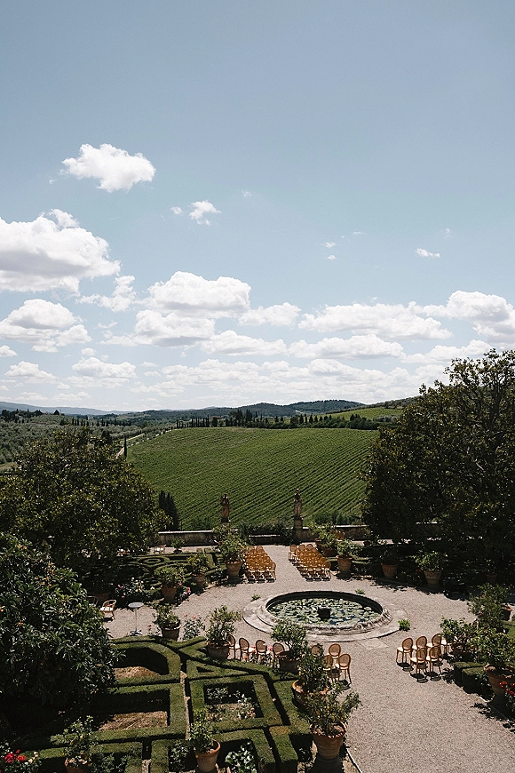 Outdoor ceremony setup with garden wedding ceremony chairs arranged symmetrically around a stone fountain with lily pads on a terrace overlooking vineyard hills