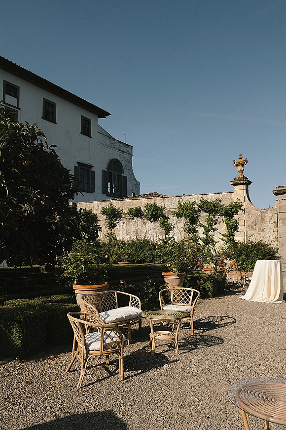 Cocktail hour patio with wedding cocktail hour seating—rattan bistro set and potted citrus trees in a gravel villa courtyard under blue sky