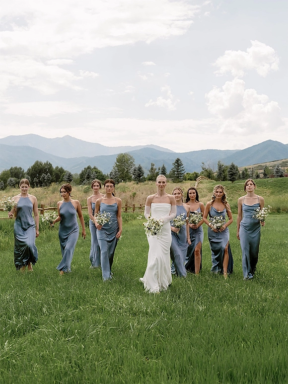 Bride with bridesmaids walking photo, bride in an off the shoulder wedding dress with bouquets in a mountain meadow under cloudy skies