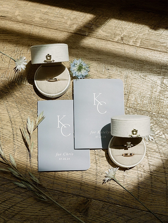 Wedding rings with diamond engagement ring and gold band resting on velvet box atop monogram invitations, lit by window shadows on wood table