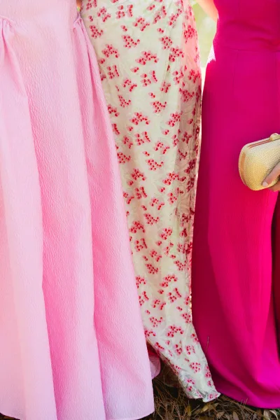 Wedding guest outfits in pink dresses, including a floral embroidered dress, styled with a gold clutch against outdoor greenery and grass