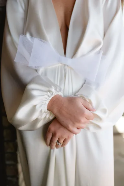 Wedding dress close-up with a tulle bow and deep V neckline, satin fabric and long sleeves highlighted in soft natural light
