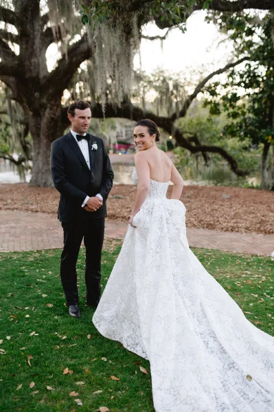 Couple portrait of bride in strapless lace wedding dress and groom in black tuxedo under an oak tree with spanish moss by a lake