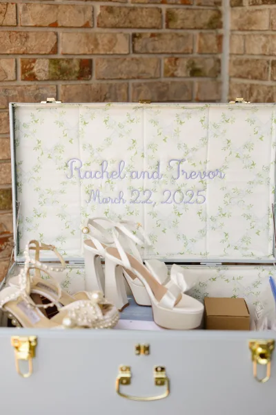 Wedding keepsake trunk with personalized wedding keepsake box embroidery, floral lining, white platform and pearl heels inside, set by a brick wall