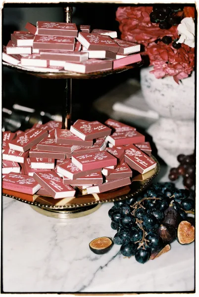 Wedding matchbooks on a two-tier stand with custom matchbooks wedding favors on a brass tray, grapes, figs, and floral decor on marble tabletop