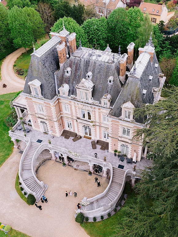Wedding venue exterior at a chateau wedding venue with stone terrace, grand staircase, and cocktail tables set in a garden courtyard