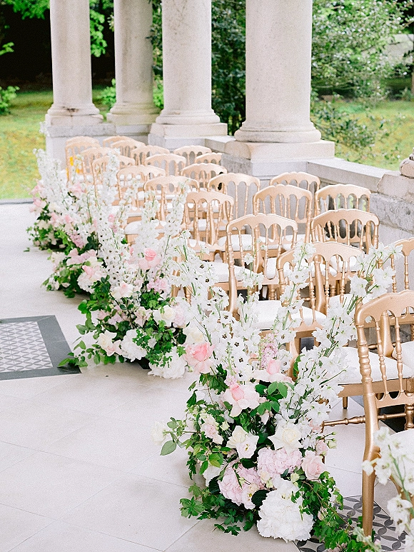 Ceremony aisle decor with wedding aisle flowers in low blush rose and white hydrangea ground arrangements beside gold chairs on a veranda